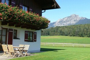 Ein Gebäude mit einem Balkon, der mit Blumen geschmückt ist, einem Tisch mit Stühlen und einem Berg im Hintergrund.