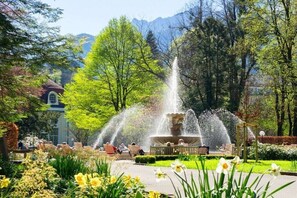A fountain surrounded by greenery and flowers, with benches and a building in the background. - Staufen in the country house Hochstaufenblick (Bayerisch Gmain)