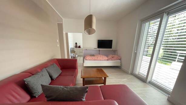 A modern living room with a red sofa, a wooden coffee table, and a TV mounted on the wall. - Open, Bright Apartment (Halle (Westfalen))