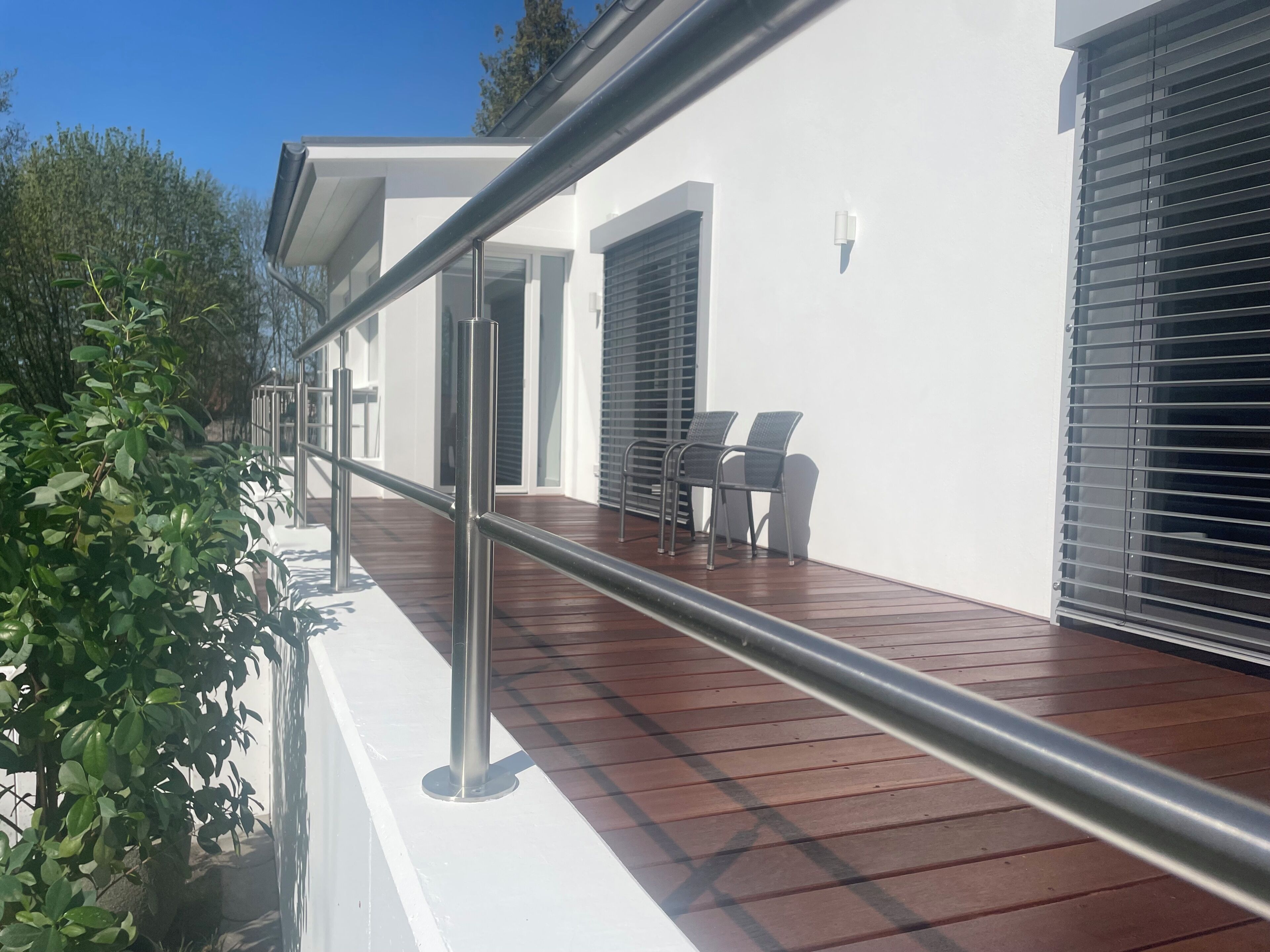 Ein Balkon mit Metallgeländer, einer Holzterrasse und zwei Stühlen.