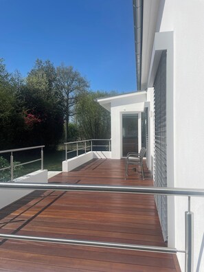 A wooden deck with metal railings, a bench, and a white building with a glass door. - Open, Bright Apartment (Halle (Westfalen))