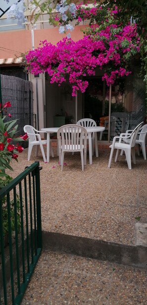 An outdoor seating area with white plastic chairs and a table, surrounded by a gravel floor and a green metal fence. - Ground-floor apartment 100 meters from the beach, ideal for families, pets welcome (La Londe-les-Maures)