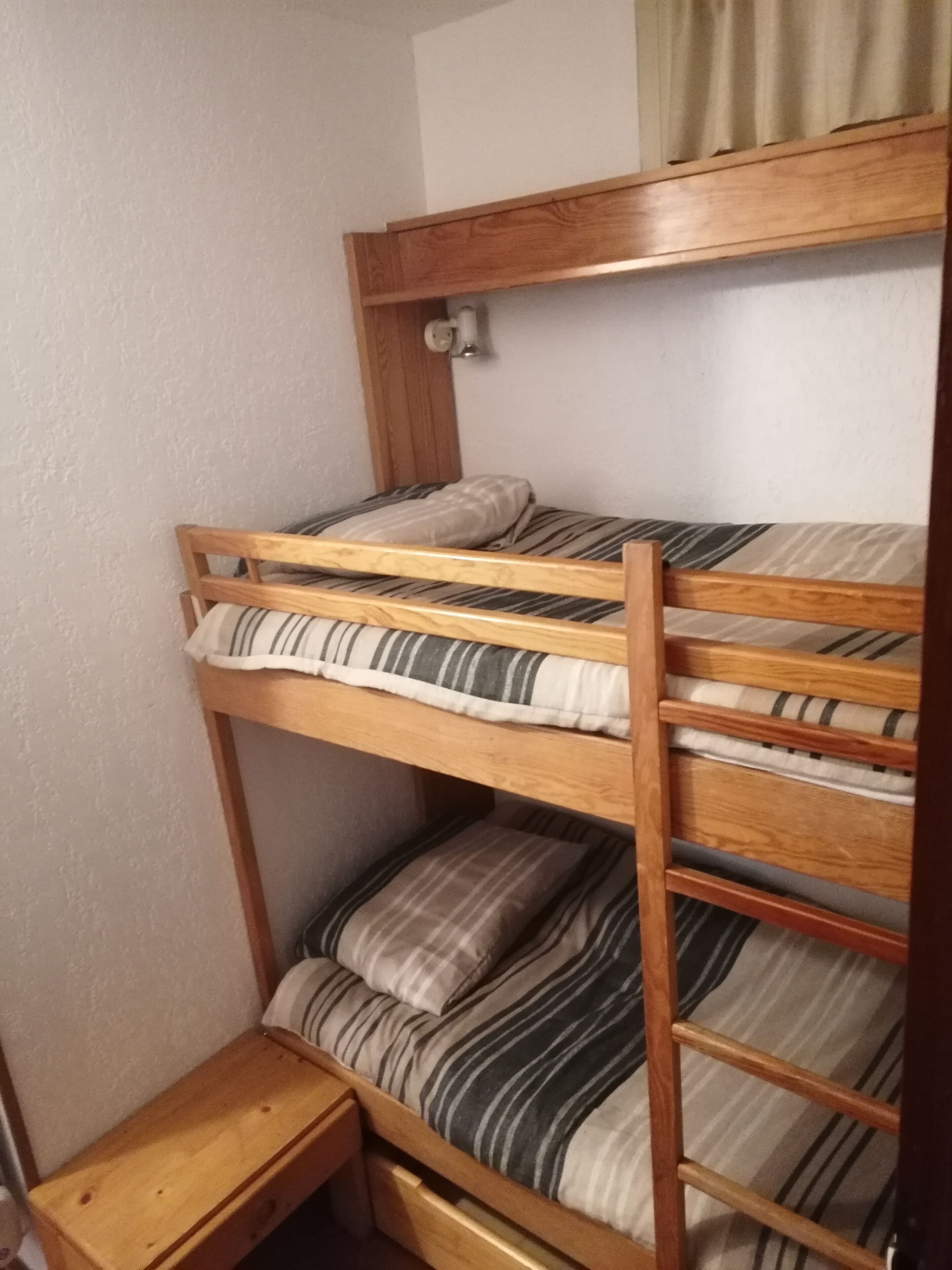 A bunk bed with striped bedding and a small wooden nightstand.