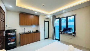 Habitación de hotel con cama, kitchenette pequeña, televisión montada en la pared y ventana con vista.
