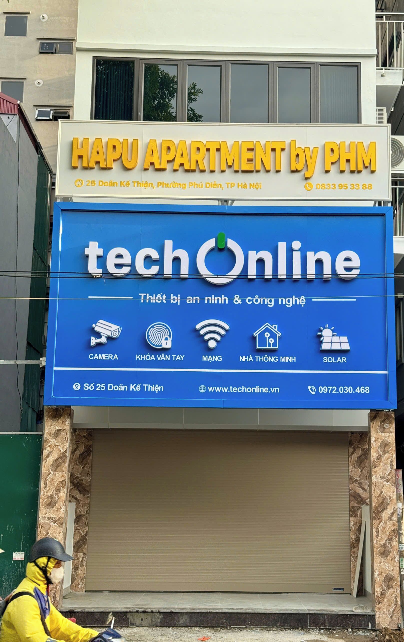 A building with a sign for 'HAPU APARTMENT by PHM' and another sign for 'techOnline' with various service icons.