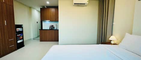 Habitación de hotel con cama, escritorio, kitchenette y unidad de aire acondicionado.