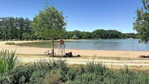 A lakeside setting with a bicycle, a ladder, and a person sitting on the sand.