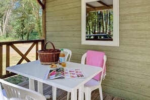 A wooden deck with a table, chairs, a wicker basket, a bottle, a glass, and a magazine.