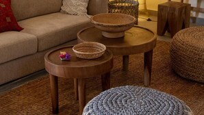 A living room with a sofa, two round wooden tables, and a woven ottoman.