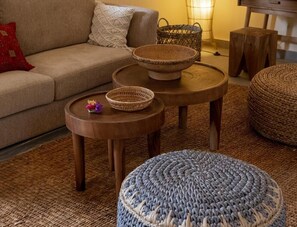 A living room with a sofa, two round wooden tables, and a woven ottoman.