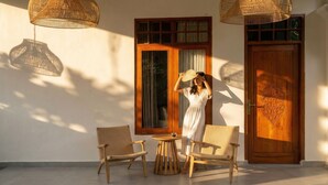A room with wicker furniture, a wooden door with an intricate design, and a window with curtains.