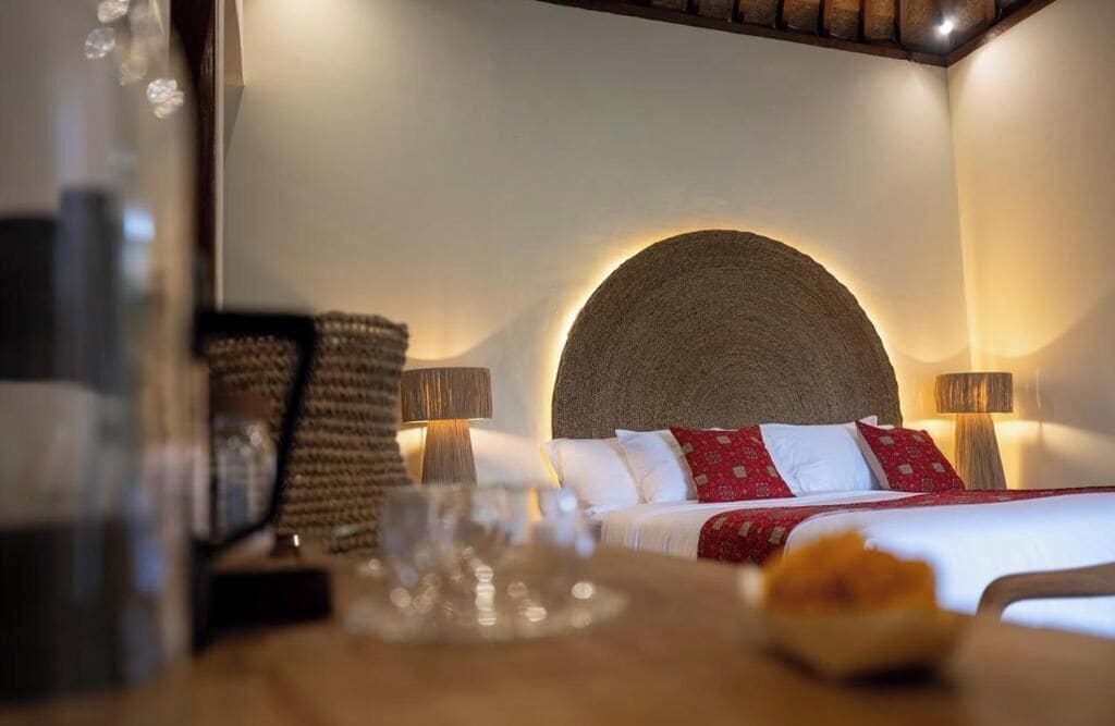 Quarto de hotel com cama, luminárias laterais e um detalhe circular na parede.