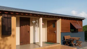 A building with a covered porch, a wooden door, and a small outdoor seating area. - "Ti Kaz Soleil" Creole House - Tropical Garden, Peace and Comfort in Sainte-Rose (Sainte-Rose)