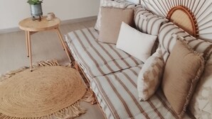A striped sofa with a woven headboard, a small wooden side table with a plant, and a round woven rug. - "Ti Kaz Soleil" Creole House - Tropical Garden, Peace and Comfort in Sainte-Rose (Sainte-Rose)