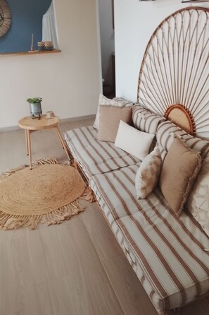 Ein gestreiftes Sofa, ein gewobener Kopfteil, ein kleiner Holztisch mit einer Pflanze und ein runder, gewobener Teppich.