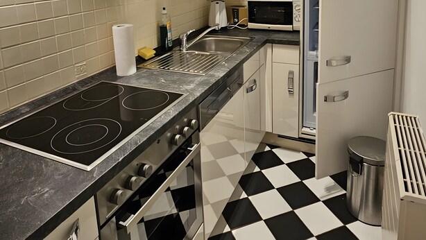 A modern kitchen with a black and white checkered floor, stainless steel appliances, and white cabinetry. - Nice small apartment for 2 in Kirkel with parking & quiet location (Kirkel)