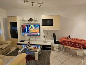 Ein Wohnzimmer mit Fernseher, einer Couch, einem Couchtisch und einem Essbereich mit Tisch und Stühlen.
