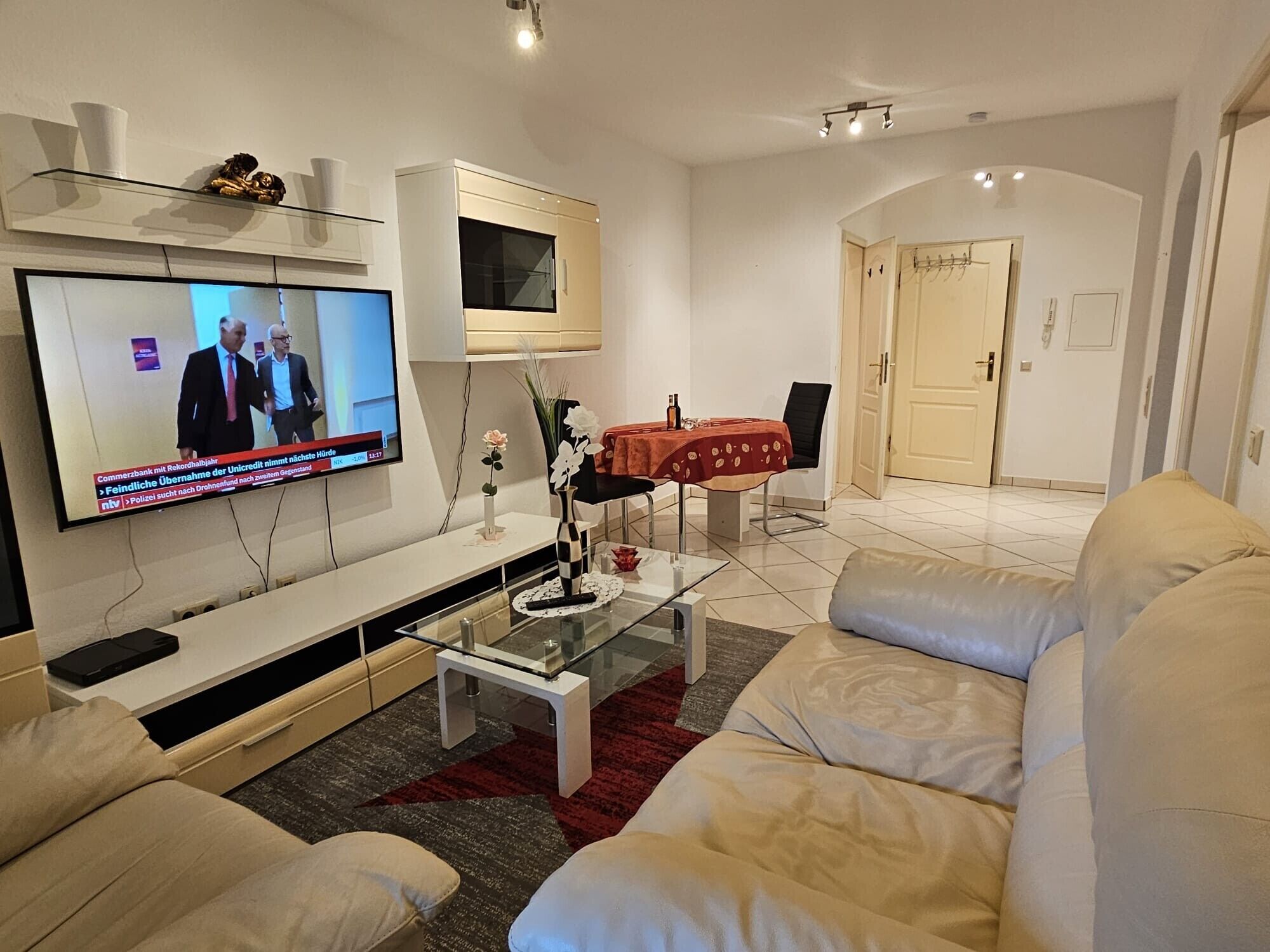 A modern living room with a flat-screen TV, a glass coffee table, and a beige sofa.