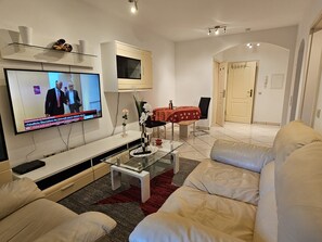 Ein modernes Wohnzimmer mit Flachbildfernseher, einem Glastisch und einem beigefarbenen Sofa.