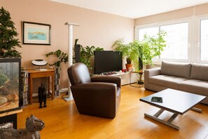A living room with a sofa, a coffee table, a TV, a bookshelf, and a fireplace. - Rooftop & Pool - Secure Parking (Paris)