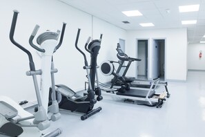 Ein Fitnessstudio mit verschiedenen Trainingsgeräten, darunter Crosstrainer und Laufband, in einem hellen Raum mit weißen Wänden und einem sauberen Boden.