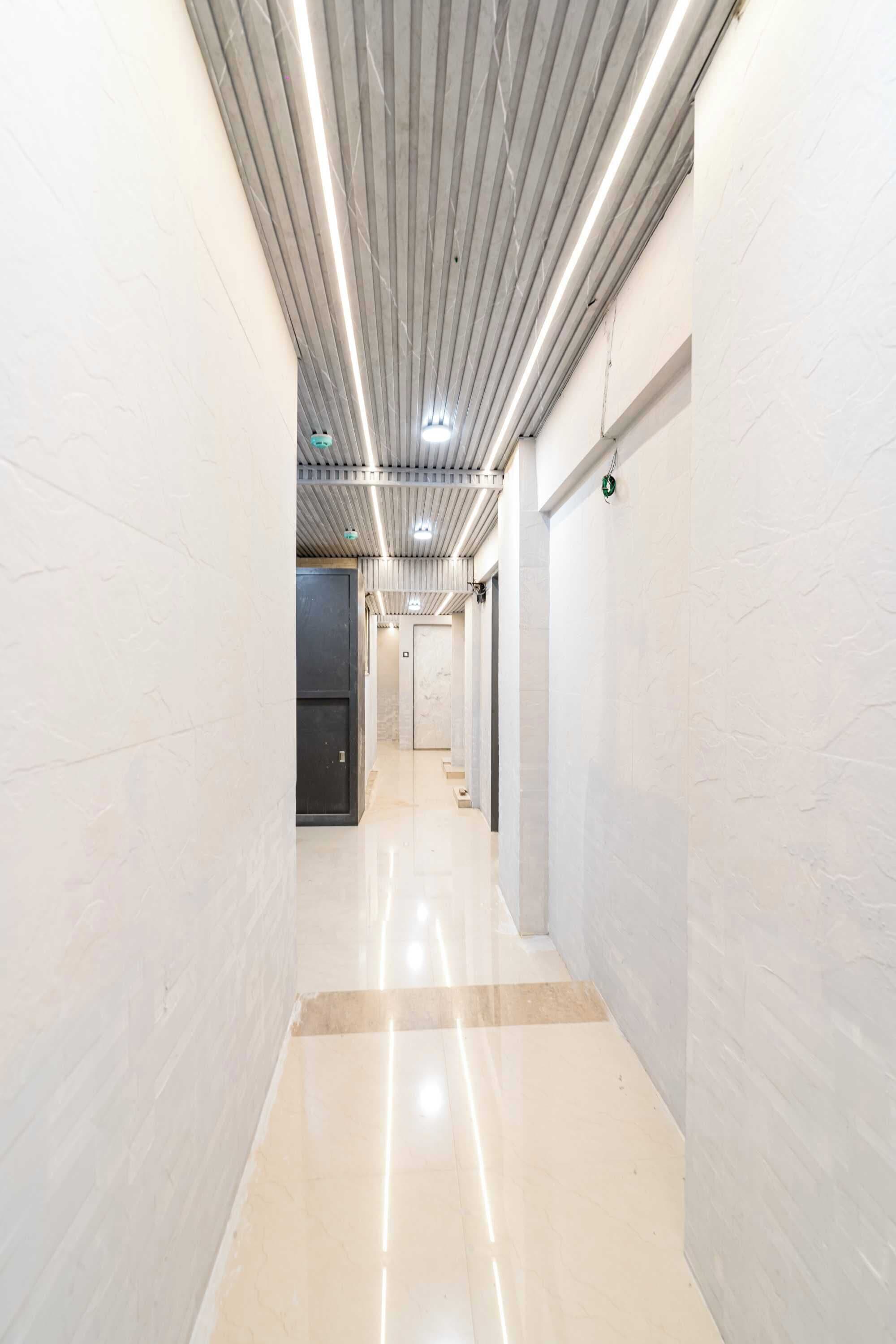 Um corredor com piso brilhante, paredes brancas e teto com luminárias lineares.