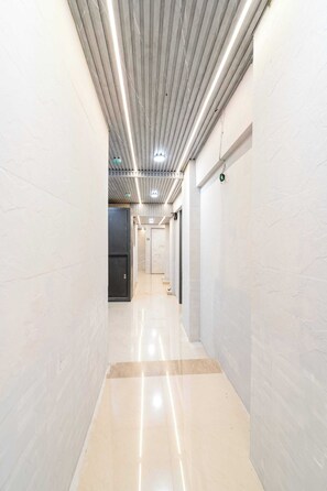 Un pasillo con piso brillante, paredes blancas e iluminación empotrada en el techo.