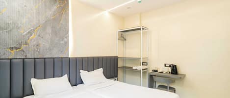 A modern hotel room with a large bed, a nightstand, a desk with a coffee maker, and a wardrobe.