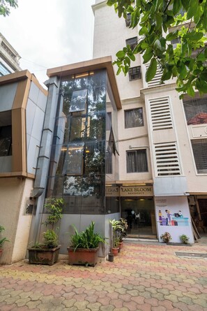 Un edificio con fachada de vidrio moderna, un letrero que dice 'Lake Bloom Residency' y plantas en macetas al frente.