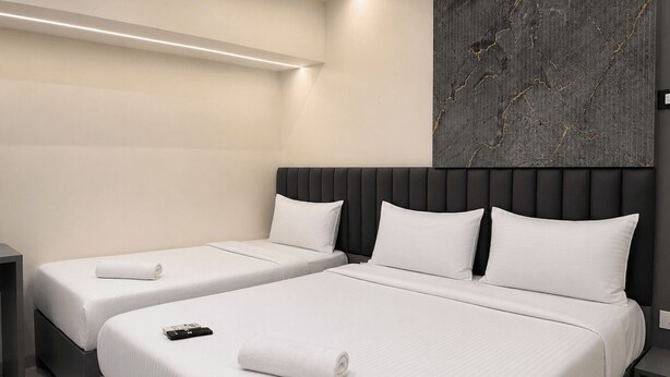 Habitación de hotel con dos camas, un cabecero moderno, una obra de arte colgada en la pared y una mesita de noche con un control remoto.