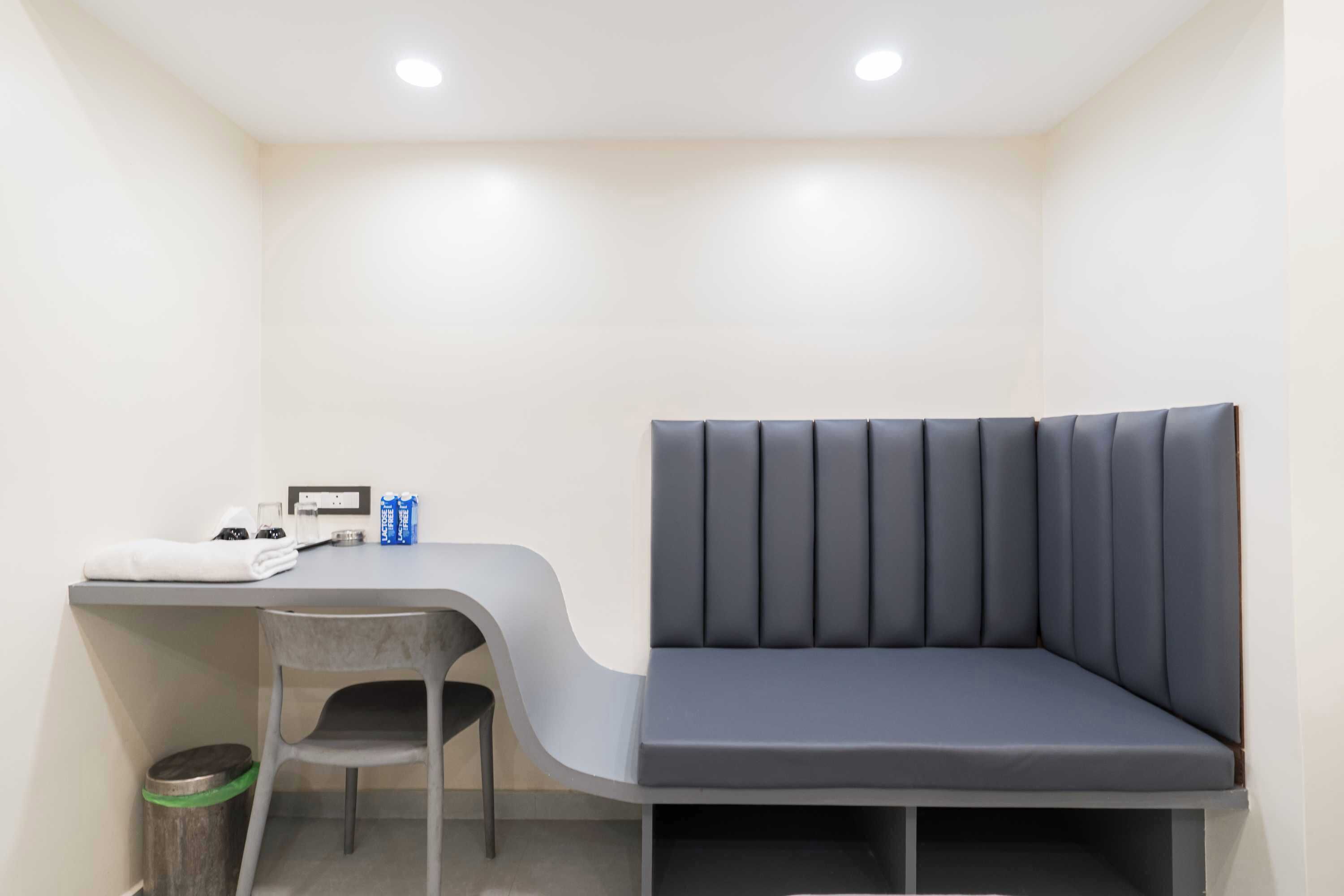 Una habitación pequeña y moderna con un banco gris, un escritorio y una silla.