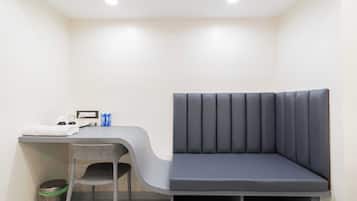 Una habitación pequeña y moderna con un banco gris, un escritorio y una silla.