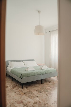 Ein Schlafzimmer mit Bett, Nachttisch, Lampe und einem Fenster mit Vorhängen.