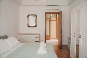 Ein Schlafzimmer mit einem Bett, einer Kommode, einem Spiegel und einer offenen Tür zu einem anderen Raum.