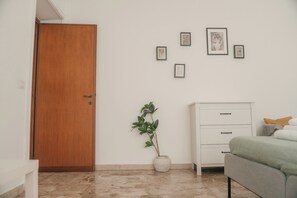 Ein Zimmer mit Holztür, weißem Schminktisch, grünem Sofa, einer Topfpflanze und mehreren gerahmten Bildern an der Wand.