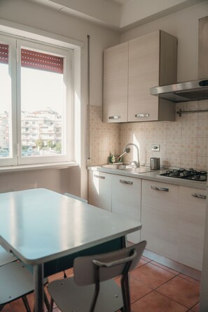 Eine Küche mit Fenster, Tisch, Stühlen, Schränken, einem Herd und einer gefliesten Spritzschutzwand.