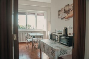 Eine Küche mit Tisch und Stühlen, einem Wasserkocher, einem Toaster und einem Fenster mit Jalousien.
