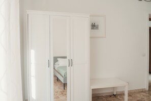 Una habitación con un armario blanco, una cama con colcha verde y una pequeña mesa blanca.