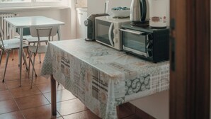 A kitchen with a table, chairs, a microwave, a kettle, and a window with blinds. - A cozy home for families and friends, just a stone's throw from the Vatican. (Roma)