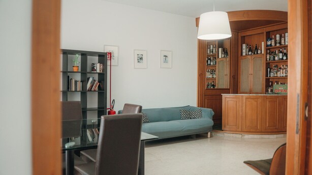 A living room with a sofa, a bookshelf, a dining table with chairs, and a cabinet with bottles. - A cozy home for families and friends, just a stone's throw from the Vatican. (Roma)