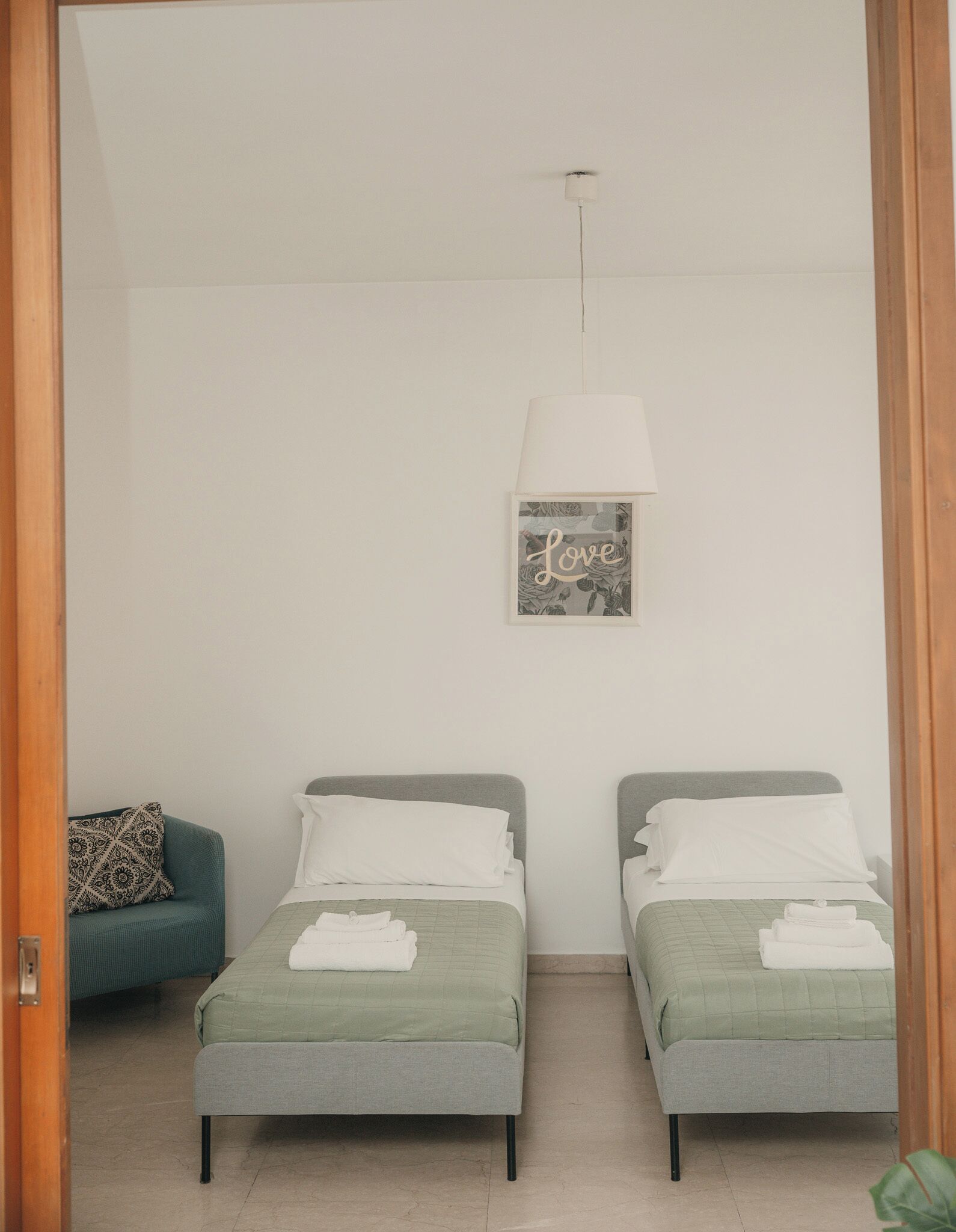 Ein Schlafzimmer mit zwei Einzelbetten, einer hängenden Leuchte und einem Wandbild mit der Aufschrift 'Love'.