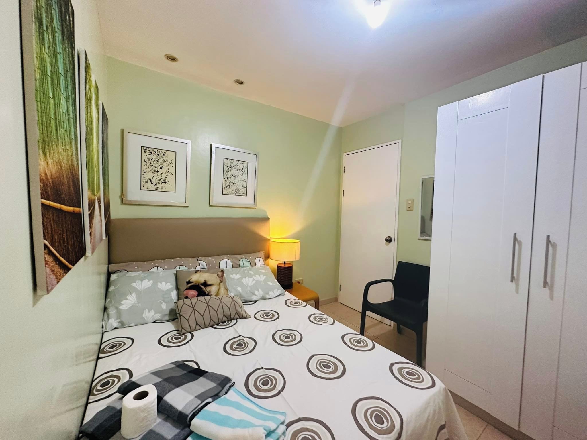 A bedroom with a bed, pillows, a nightstand, a lamp, a chair, and a wardrobe.