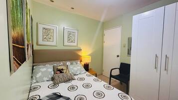 A bedroom with a bed, pillows, a nightstand, a lamp, a chair, and a wardrobe.