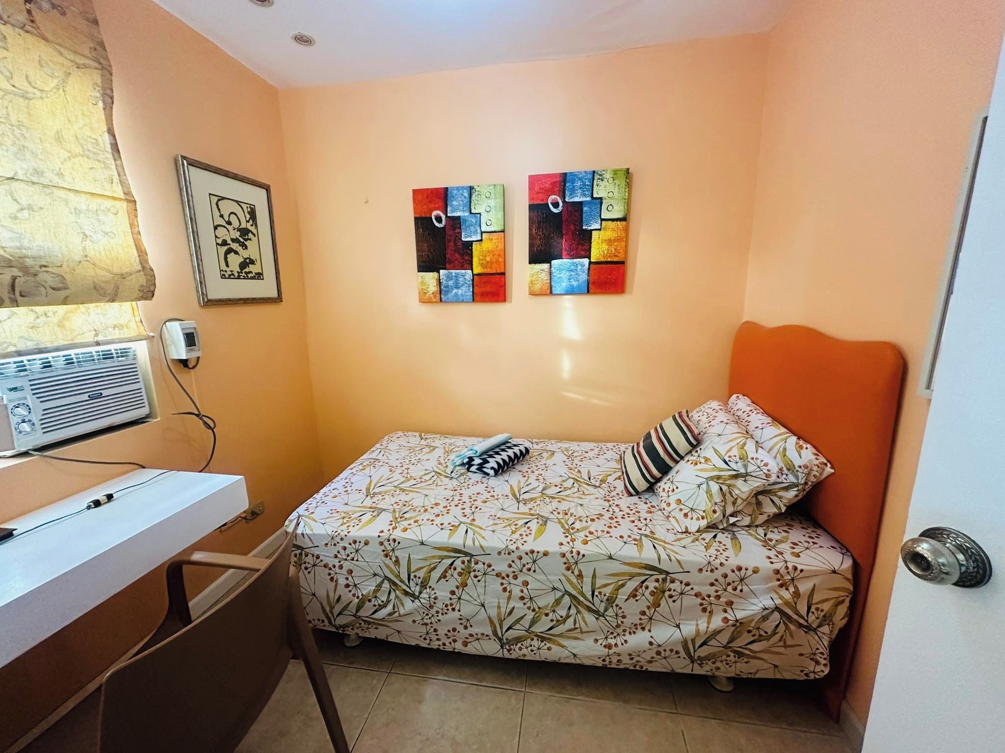 Une petite chambre à coucher comprenant un lit, un bureau et deux tableaux accrochés au mur.