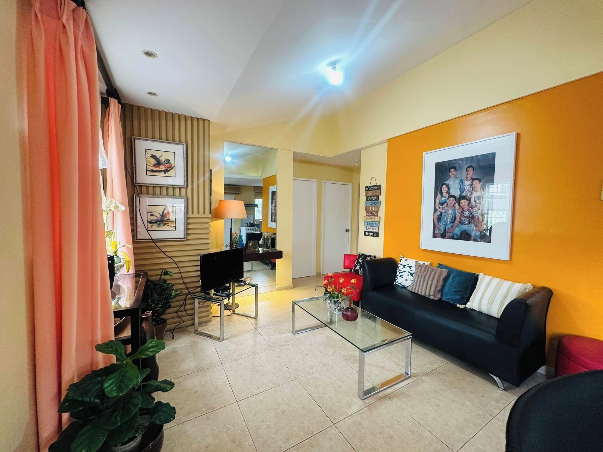 A living room with a sofa, coffee table, and a TV. There is a kitchen in the background.
