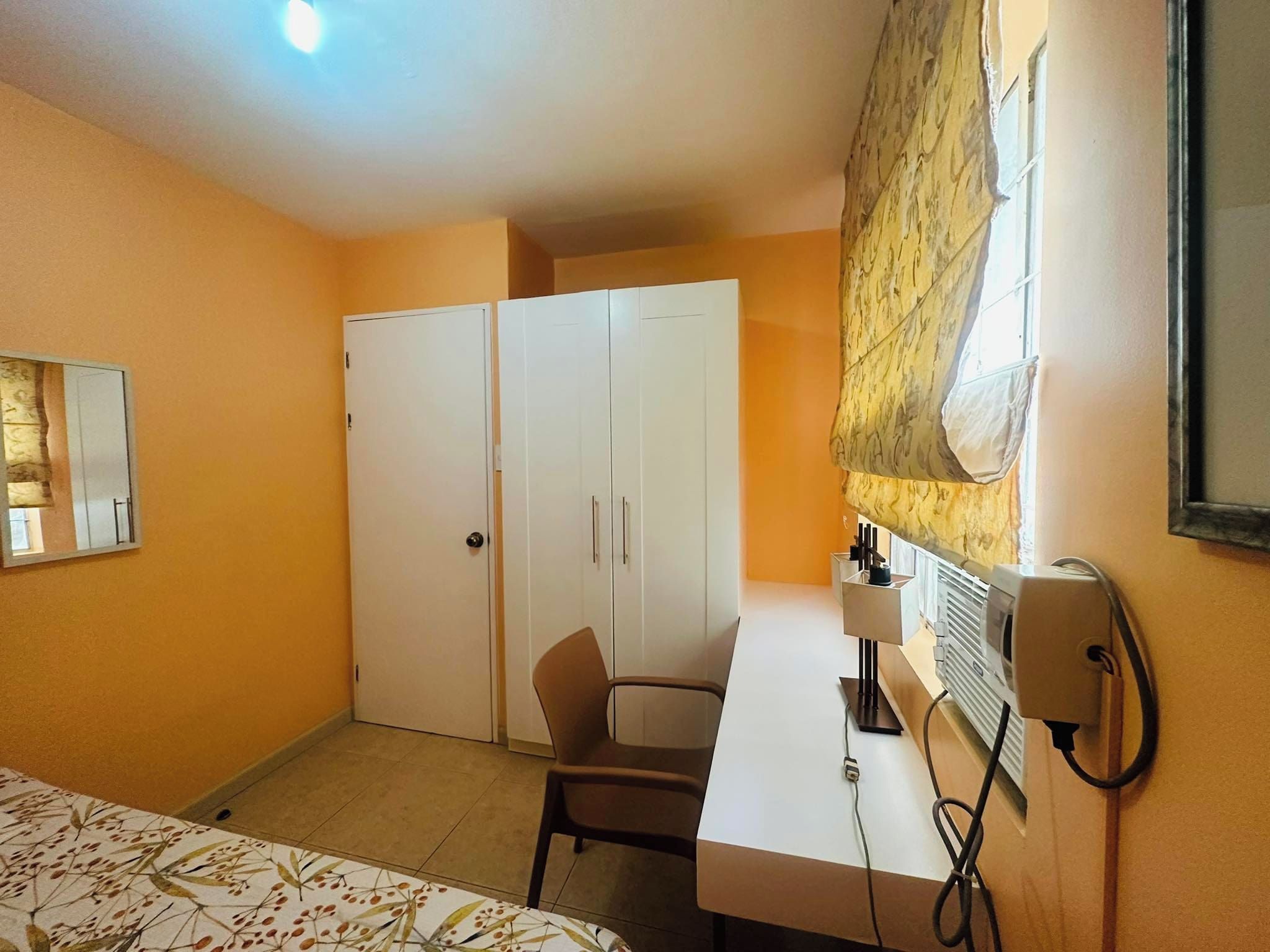 Habitación de hotel con cama, escritorio, silla, armario y ventana con cortinas.