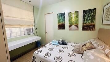 A bedroom with a bed, a window with blinds, a wall-mounted air conditioner, and three framed pictures.
