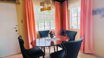 Un comedor con una mesa redonda, cuatro sillas, un jarrón con flores y un ventilador.