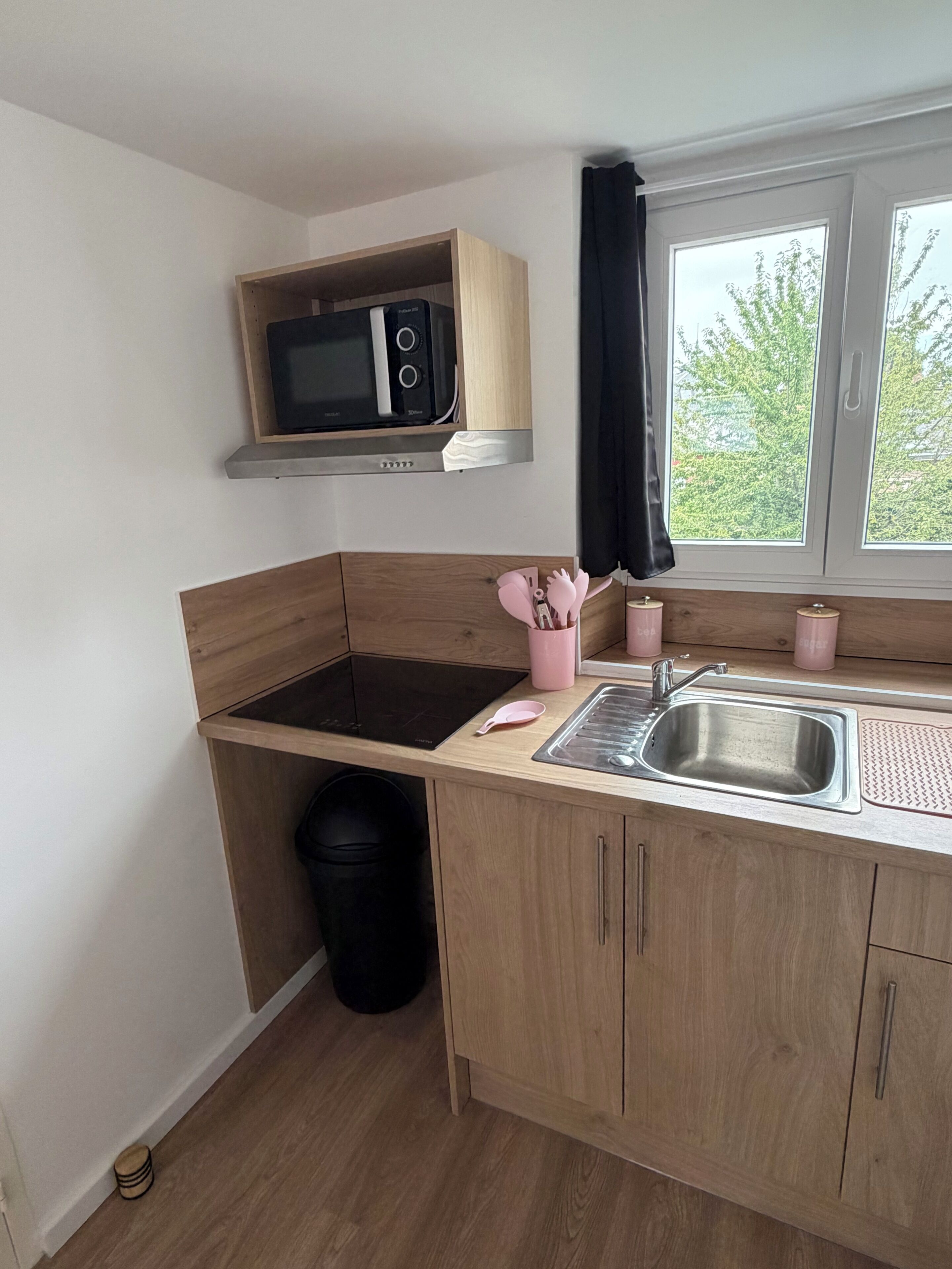 Cocina compacta con microondas, lavamanos y armarios de madera.