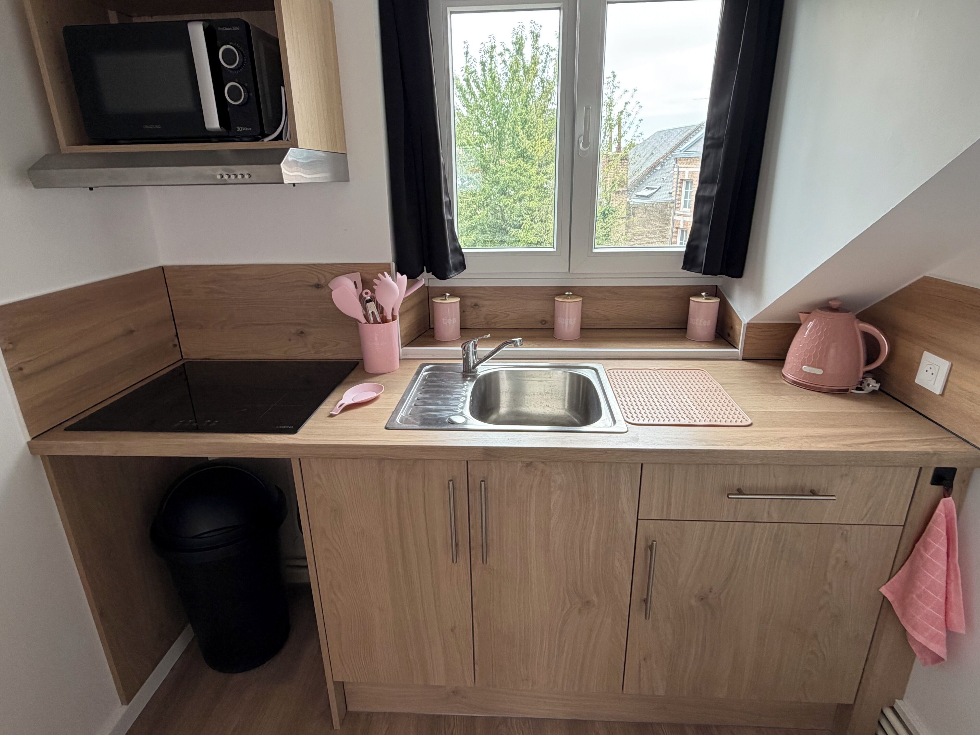 A compact kitchen with a microwave, sink, and wooden cabinets.